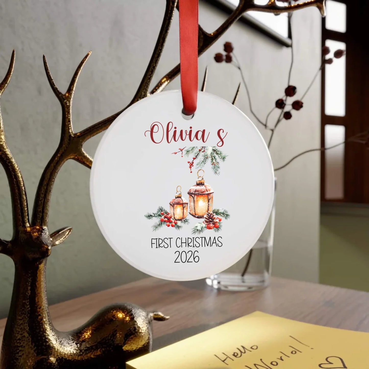 Personalized Christmas ornament with 'Olivia's First Christmas 2026' text, hanging on a branch.
