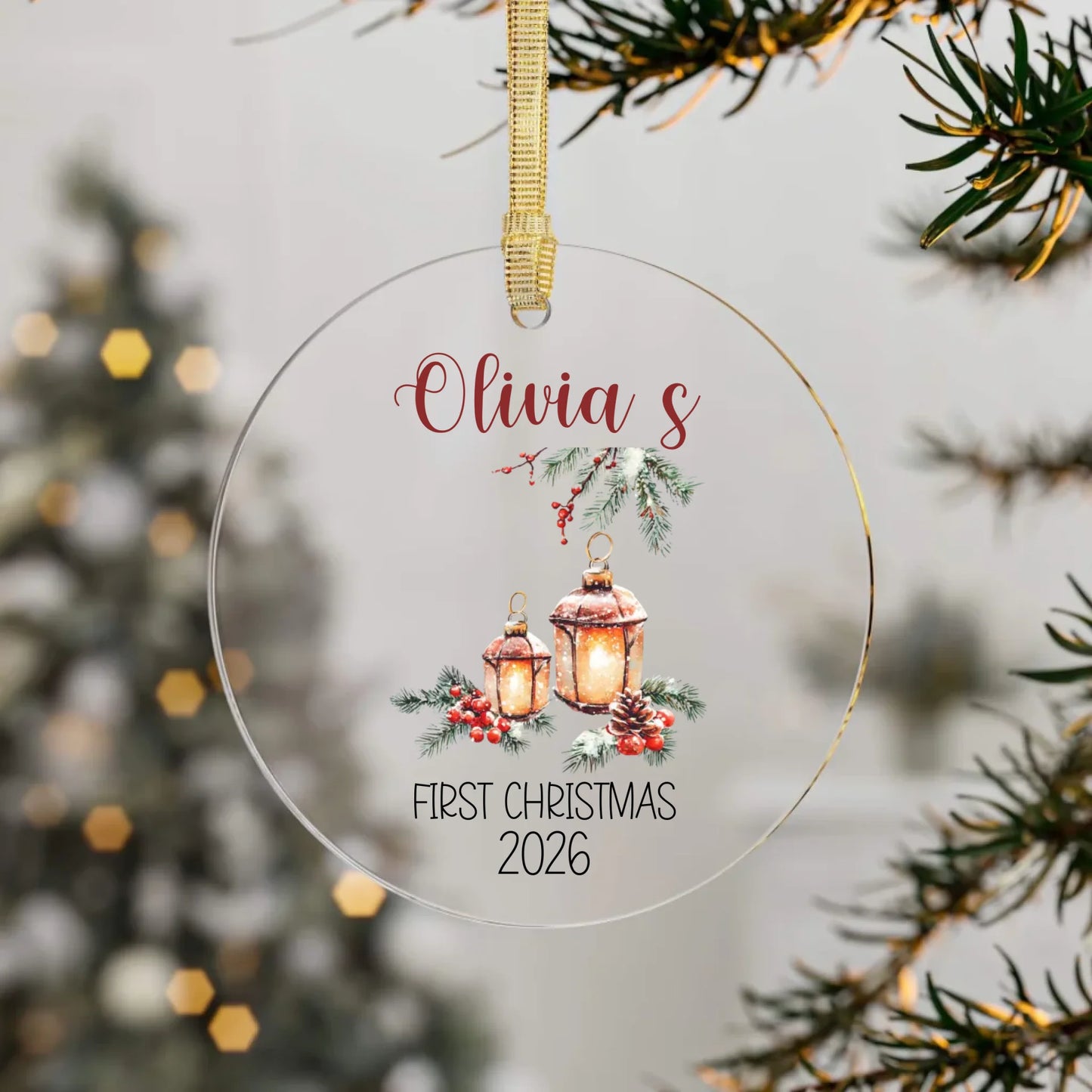 Personalized Christmas ornament with lanterns and 'Olivia's First Christmas 2026' text, hanging on a tree branch.