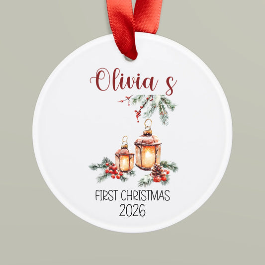Round Christmas ornament with lanterns and 'Olivia's First Christmas 2026' text on a gray background